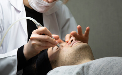 Professional beautician is rejuvenating male face by cavitation laser apparatus. Man is lying on massage table and relaxing