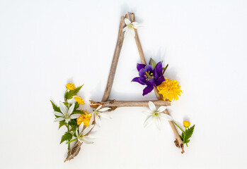 Letter A is made of tree branches decorated with flowers, a product from natural materials on a white background.
