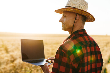 Wall Mural - Image of adult man working with laptop while standing at cereal field