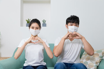 Asian couple wearing protective face mask and making shape of Heart by their Hands at home.