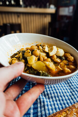 Poster - Waiter serving chickpea stew with chard, boiled egg and potatoes on a blue checkered tablecloth, bread