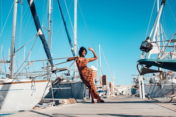 Wall Mural - Happy and cheerful young black woman say ahllo standing on the dock with lot of boats around - concept of travel and summer holiday vacation for people and tourism