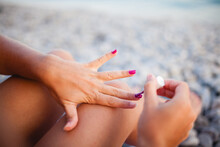 Young Woman Applying Nail Polish On The Beach On A Sunny Summer Day
