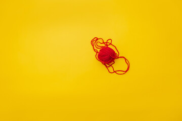 on a yellow background is a red ball of woolen thread, the thread is slightly unraveled and lies on the ground