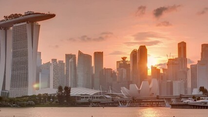 Wall Mural - Sunset over the downtown skyline of Singapore as viewed from across the water from The Garden East timelapse. Sun behind skyscrapers. Singapore. Reflection in water