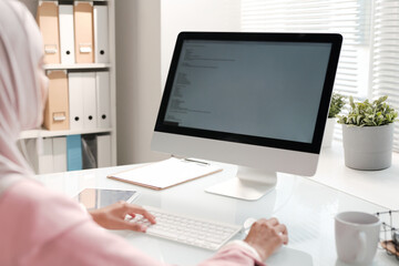 Wall Mural - Over shoulder view of Muslim programmer sitting at office table and coding information for website using computer