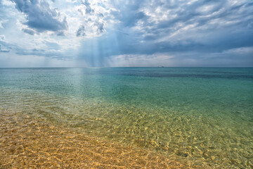 transparent turquoise sea with dramatic cloudy sky with sun rays