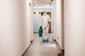 Wall Mural - Full length of man in sterile suit disinfecting hall of the building. Protection from corona concept.