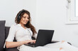 © Bojan Topalovic - Smiling girl in white clothes lying on the couch, wearing headphones and typing on laptop.