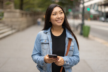 Wall Mural - Young Asian woman walking street texting cellphone