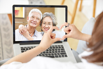 Canvas Print - young asian woman forming a heart shape while talking chatting with parents via video call using laptop