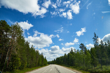 View from relief car windscreen on the blue sky with white clouds, grey asphalt road and landscape with forest and green teeses. Landscape through window