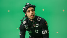 Portrait Of An Actor Wearing Motion Caption Suit And Head Rig Posing With Green Screen Background. Big Budget Filmmaking On Film Studio Set Shooting Blockbuster Movie With Chroma Key.