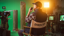 Prominent Successful Senior Director Is Sitting At His Chair And Commands "Action!" To Start Shooting. On The Studio Film Set With High End Equipment Professional Crew Shooting High Budget Movie