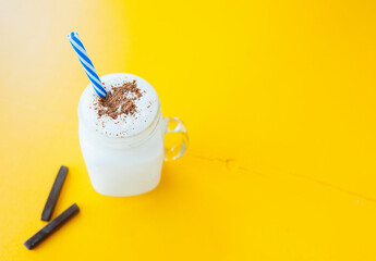 milkshake in glass mug witha handle and blue straw, sprinkled with chocolate on bright yellow background, minimalistic style