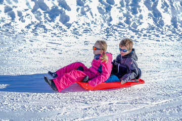 Two joyful kids sledding down the hills on a winter day. Brother and sister