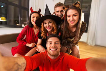 Sticker - friendship, holiday and people concept - group of happy smiling friends in halloween costumes of vampire, devil, witch and cheetah taking selfie at home party at night