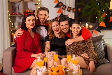 Sticker - friendship, holiday and people concept - group of happy smiling friends in halloween costumes of vampire, devil, witch and cheetah at home party at night