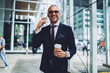 © BullRun - Successful male entrepreneur in stylish sunglasses talking on phone about business ideas for startup, happy bankier informal war having  mobile conversation during work break holding coffee to go