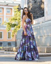 Fashion Portrait Of Young Beautiful Woman With Brunette Hair Wearing Long Blue Colorful Dress And Sunglasses And Walking In City. Fashionable Stylish Full Length Outdoor Portrait Of Female Model