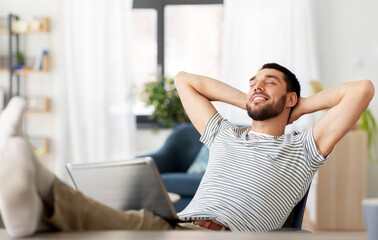 Canvas Print - remote job and business concept - happy smiling man with laptop computer resting feet on table at home office