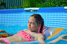 Close-up - A Girl In A Pink Bathing Suit Lies On An Inflatable Mattress In A Blue Pool, Closing Her Eyes And Sunbathing