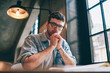 Portrait of serious hipster guy sitting at table and looking at camera indoors, concentrated man have doubt about preparing for exam looking at camera during break of learning at university campus
