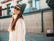 © halayalex - Portrait of beautiful smiling model. Female dressed in warm hipster white sweater and beanie. Trendy girl posing in the street at sunset. Funny and positive woman having fun outdoors in sunglasses