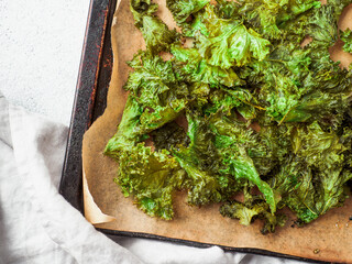 Green Kale Chips with salt on oven-tray. Homemade healthy snack for low carb, keto, low calorie diet. Gray cement background. Ready-to-eat kale chips, copy space for text