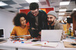 © BullRun - Positive young people dressed in casual wear laughing during teamwork at meeting table with laptop computer.Cheerful diverse hipster guys collaborating during studying courses in modern office