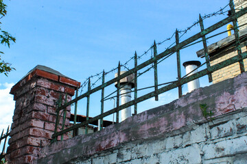 A stone fence with barbed wire at the top against a beautiful blue sky