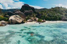 "La Digue" Island In Seychelles. Silver Beach With Granitic Stone, And Jungle. Man Enjoying Vacations On The Beach And Having Fun With Kayak. Aerial View Shot With Drone