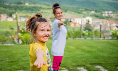 Mother and daughter doing yoga exercises outdoor - young woman doing fitness exercises in the park - Reach harmony