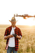 © Drobot Dean - Image of happy handsome man using drone while standing at cereal field