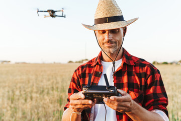 Wall Mural - Image of pleased handsome man using drone while standing at cereal field