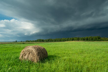 Storm Cloud Over Green Meadow With Hay Bales