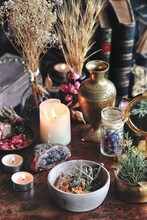 Dried Plants, Herbs And Yellow Rose Flower Petals In A Grey, Dirty Clay Pot. Wiccan Witch Altar With Ingredients On It Ready To Make Cast A Spell. Evergreens, Books, Burning Candles In Dark Background