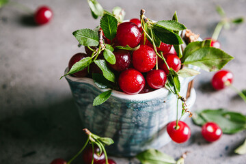 Fresh cherries with leaves and water droplets in a ceramic cup on a gray background.