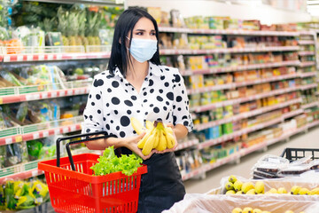 young woman in a disposable medical mask is shopping at the supermarket. buying fruit