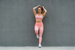 © Carlos Rodelas/ADDICTIVE STOCK - Full body of fit female athlete in sports wear and sneakers standing leaned on one leg on embankment near grey wall and looking away