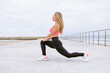 © Carlos Rodelas/ADDICTIVE STOCK - Young slim female athlete in sportswear doing side lunge while stretching legs on pavement near fence on sea coast under cloudy sky and looking away