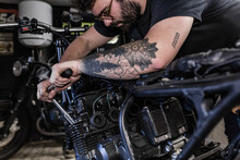 Side View Of Crop Male Mechanic Using Socket Wrench And Fixing Motorbike In Workshop