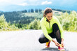 © Vadim Pastuh - Athletic young woman tie shoelaces before jogging outdoors. A girl in neon green long sleeve t-shirts with a mountains on the background. Sporty lifestyle concept