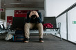 © Jake Jakab/ADDICTIVE STOCK - Full length faceless depressed exhausted male traveler in casual wear sitting on seats with head in hands in modern airport departures waiting area