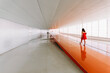 © Javier Bravo/ADDICTIVE STOCK - Back view of unrecognizable female standing on shiny orange floor of passage in modern building