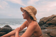 © Jorge Moya/ADDICTIVE STOCK - Side view of carefree happy asian female tourist sitting on stone looking away admiring spectacular seascape while relaxing on shore during summer holiday