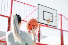 Back View Of Young Sporty Woman Performing Shot While Playing Basketball Alone On Sports Ground