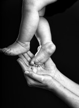 Black And White Of Crop Woman Touching Tiny Feet Of Anonymous Baby In Studio