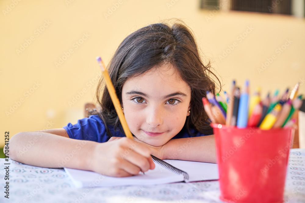 Positive school aged girl looking at camera and smiling while sitting ...