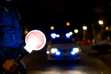 Side view of crop policeman wearing uniform with illuminated stop sign standing on street with patrol car